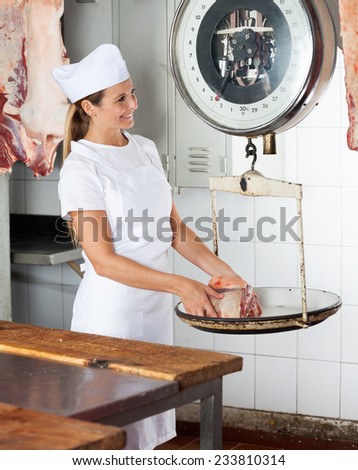 Mature female butcher weighing meat on scale at counter in butchery