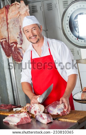 Portrait of happy male butcher cutting meat with knife in butchery