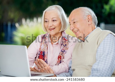 Senior couple video chatting on laptop while sitting at nursing home porch