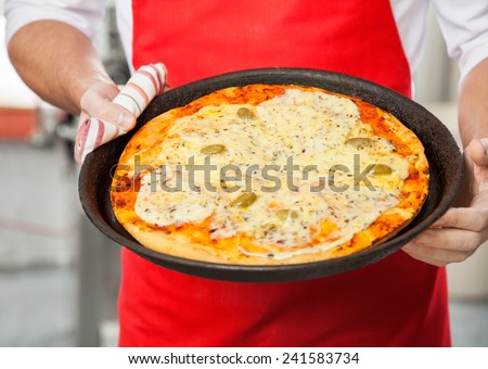 Midsection of male chef holding delicious pizza in pan at commercial kitchen