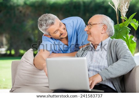 Smiling male nurse assisting senior man in using laptop at nursing home porch