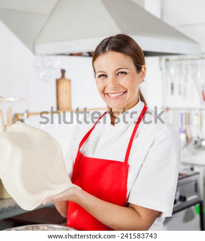 Portrait of happy female chef holding pasta sheet in commercial kitchen