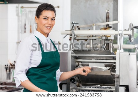 Portrait of happy female chef processing ravioli pasta in machine at commercial kitchen