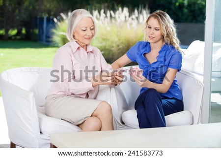 Care aid playing card game with senior woman in retirement home.
