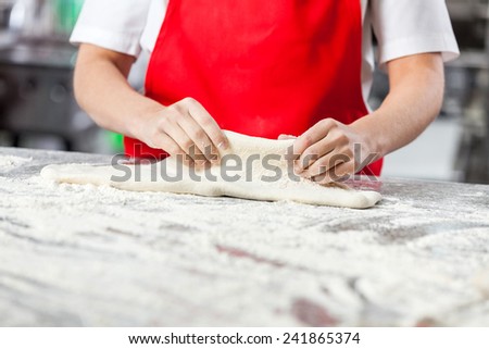 Midsection of young female chef kneading dough at messy counter in commercial kitchen