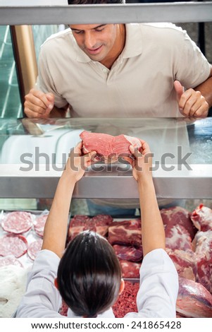 High angle view of female butcher showing fresh red meat to male customer at display counter