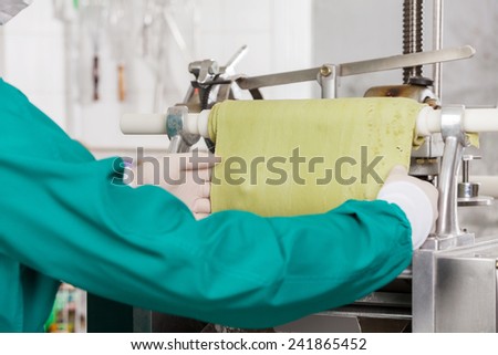 Cropped image of male chef processing green pasta sheet in machine at commercial kitchen