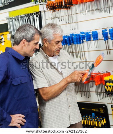Senior customer examining packed screwdriver while vendor looking at it in hardware shop