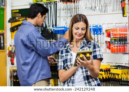 Mid adult female customer looking at packed product with man in background at hardware store