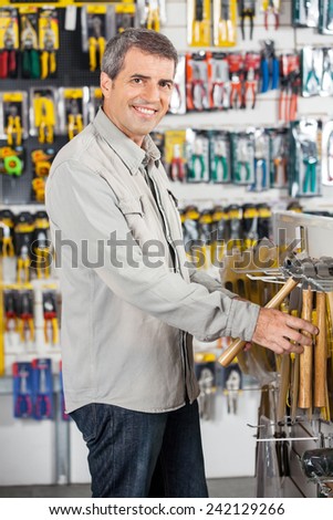 Portrait of happy mature man buying hammer in hardware store