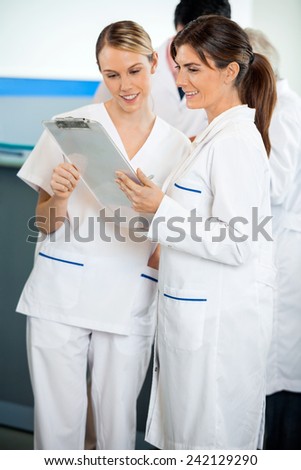 Happy female technicians reading clipboard in hospital