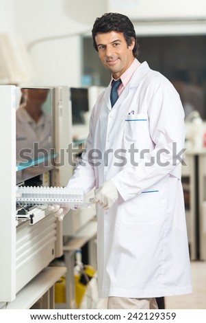 Portrait of confident male technician loading samples in analyzer at laboratory