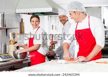 Happy chefs conversing while preparing pasta in commercial kitchen