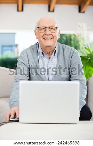 Portrait of happy senior man with laptop sitting on couch at nursing home porch