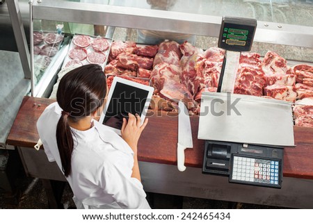 High angle rear view of female butcher using digital tablet at display counter in butchery