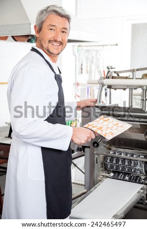 Side view portrait of happy chef using ravioli pasta machine at commercial kitchen