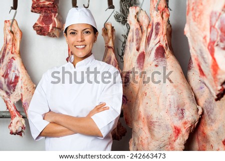 Portrait of happy female butcher standing arms crossed in slaughterhouse
