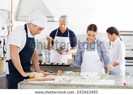 Male and female chefs making pasta together in commercial kitchen