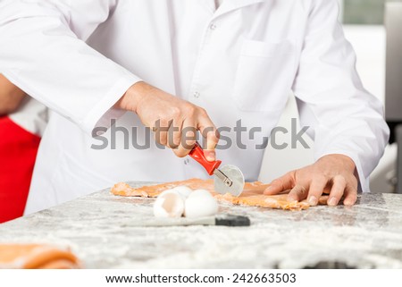 Midsection of male chef cutting ravioli pasta at messy counter in commercial kitchen