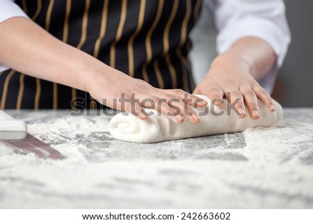 Midsection of female chef kneading dough at messy counter in commercial kitchen