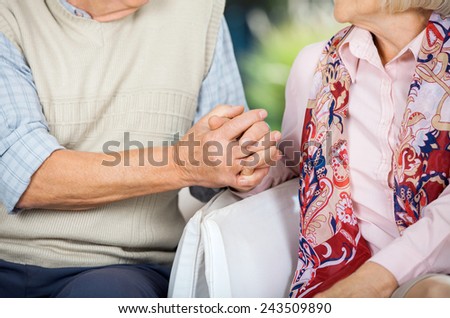 Midsection of senior couple holding hands while sitting on chairs at nursing home porch