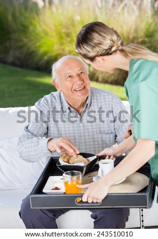Female caretaker serving breakfast to senior man at nursing home Female caretaker serving breakfast to senior man at nursing home