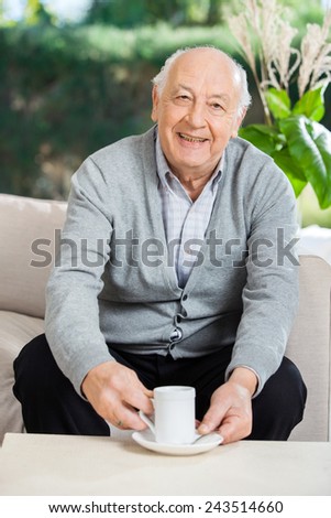 Portrait of happy senior man having coffee on couch at nursing home porch