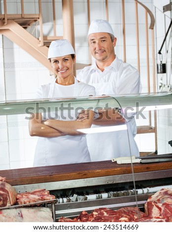 Portrait of confident male and female butchers standing at meat counter in shop