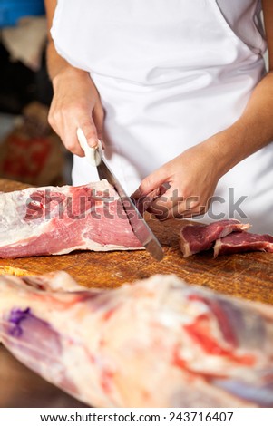 Midsection of female butcher cutting raw meat at counter in shop