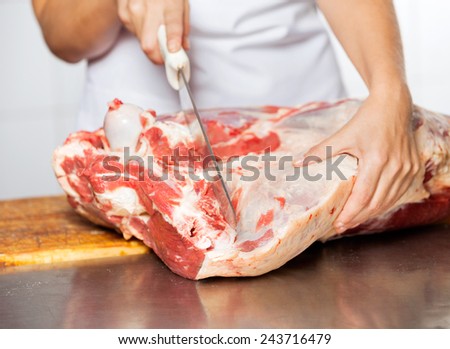 Cropped image of butcher cutting raw meat with knife at counter in shop