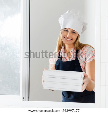 Portrait of happy young female chef holding packed pasta boxes at window