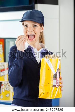 Portrait of young female worker eating popcorn from paperbag at cinema concession stand