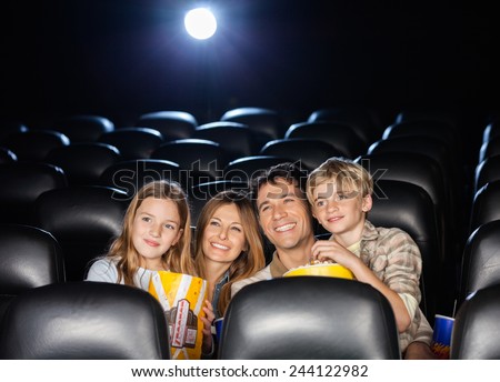 Happy family of four having snacks while watching film in movie theater