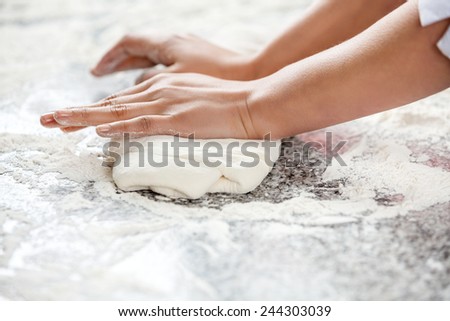 Cropped image of female chef\'s hands kneading dough at messy counter in commercial kitchen