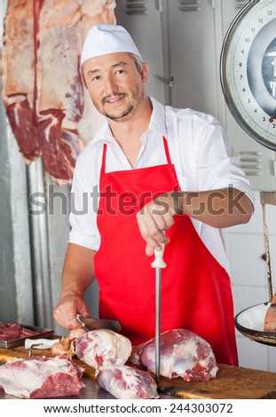Portrait of confident male butcher with knife and sharpener in butchery