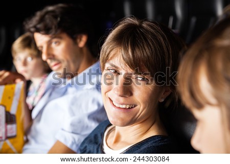 Happy woman talking to daughter while watching movie with family in cinema theater