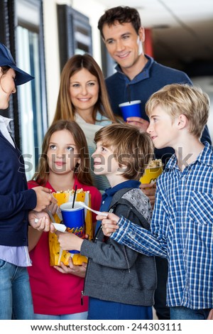 Young female worker taking movie tickets from family at cinema