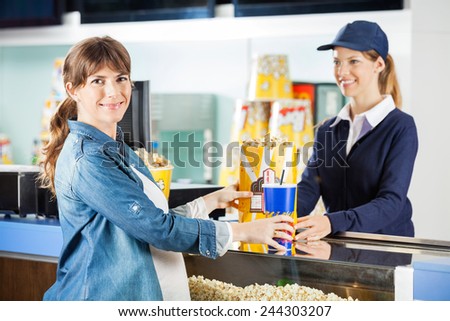 Portrait of smiling pregnant woman buying popcorn and drink from seller at cinema concession counter