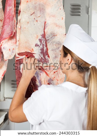 Rear view of female butcher analyzing raw meat hanging in shop