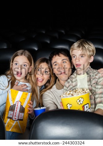 Surprised family of four with popcorn watching movie in cinema theater