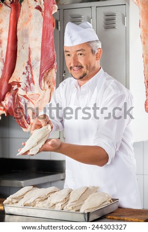 Mature male butcher giving chicken pieces covered with flour in shop