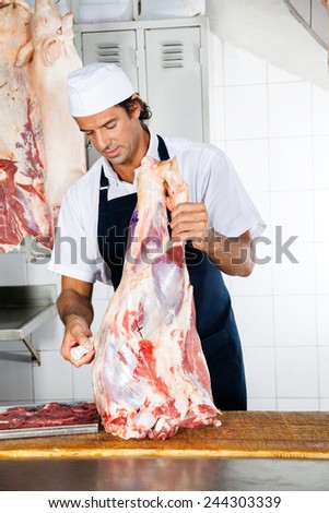 Male butcher with meat working at counter in shop
