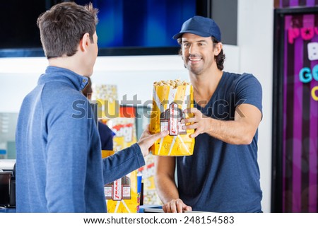 Smiling male worker selling popcorn to man at cinema concession stand