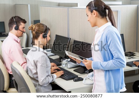 Female customer service executive holding digital tablet while talking to colleagues working in call center