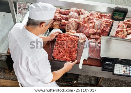 High angle view of butcher holding minced meat tray at display cabinet in butchery