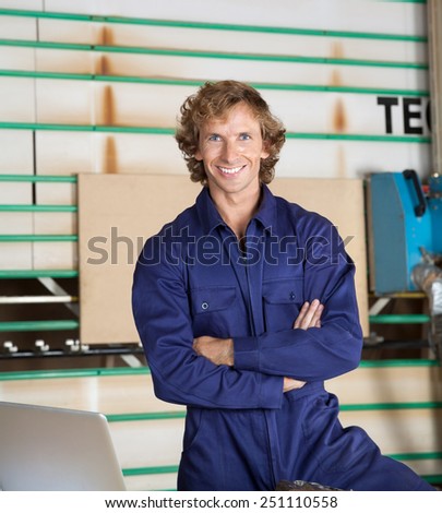 Portrait of confident carpenter in uniform standing arms crossed against vertical panel saw