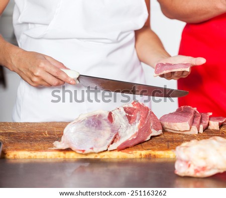 Midsection of female butcher holding knife and fresh meat piece at counter in shop