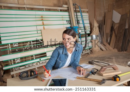 Happy female carpenter working on blueprint while looking away in workshop