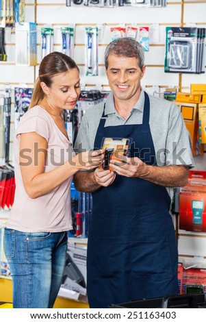Salesman assisting female customer in buying flashlight at hardware store