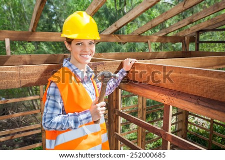 Portrait of confident female construction worker holding hammer in timber frame at site
